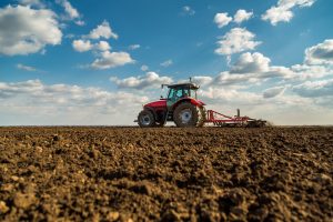 Farmer in tractor preparing land with seedbed cultivator as part of pre seeding activities in early spring season, representing agricultural vehicle insurance..